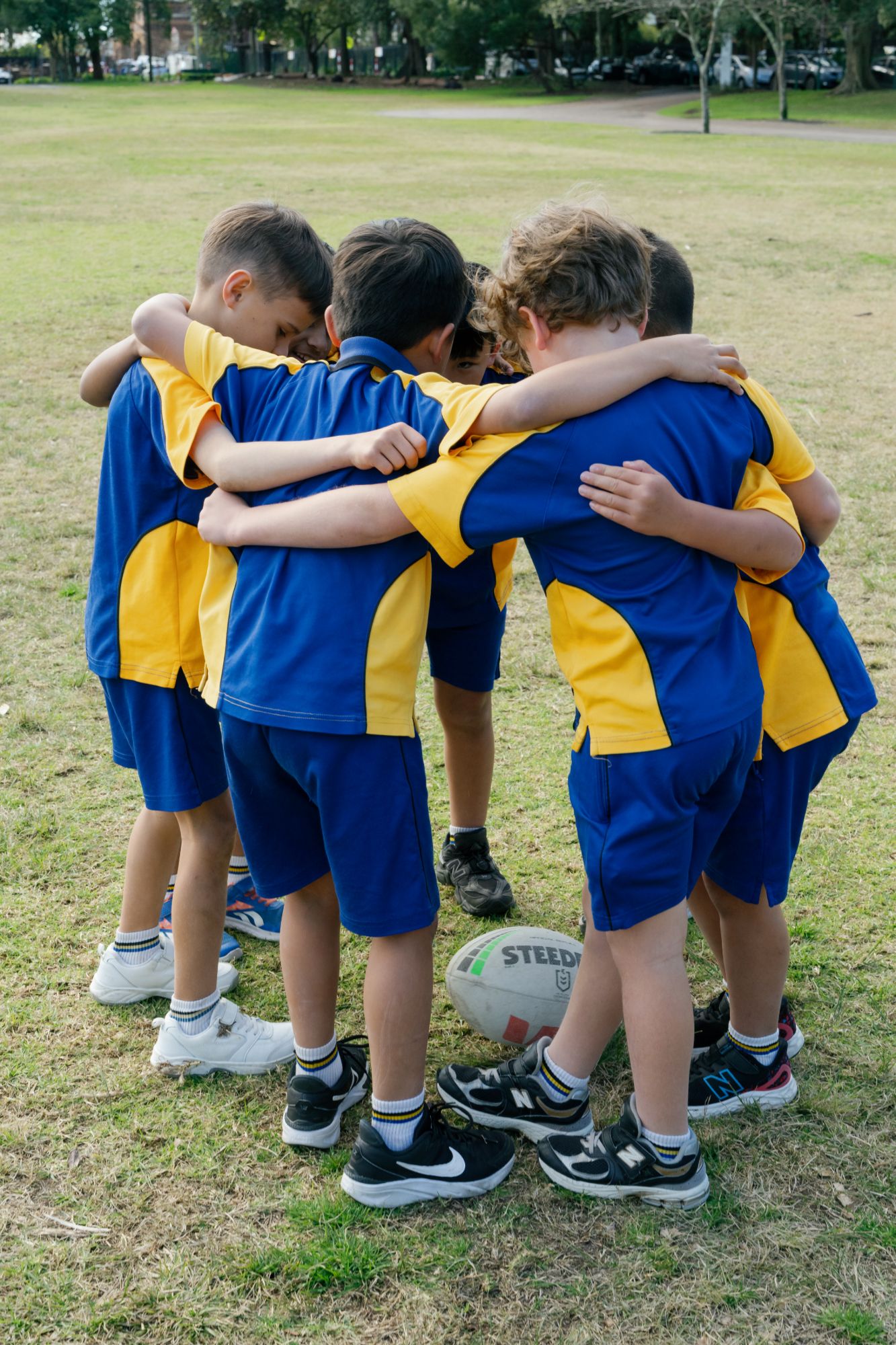 Coogee Prep boys in their blue and gold sports uniforms in a team huddle around a rugby ball