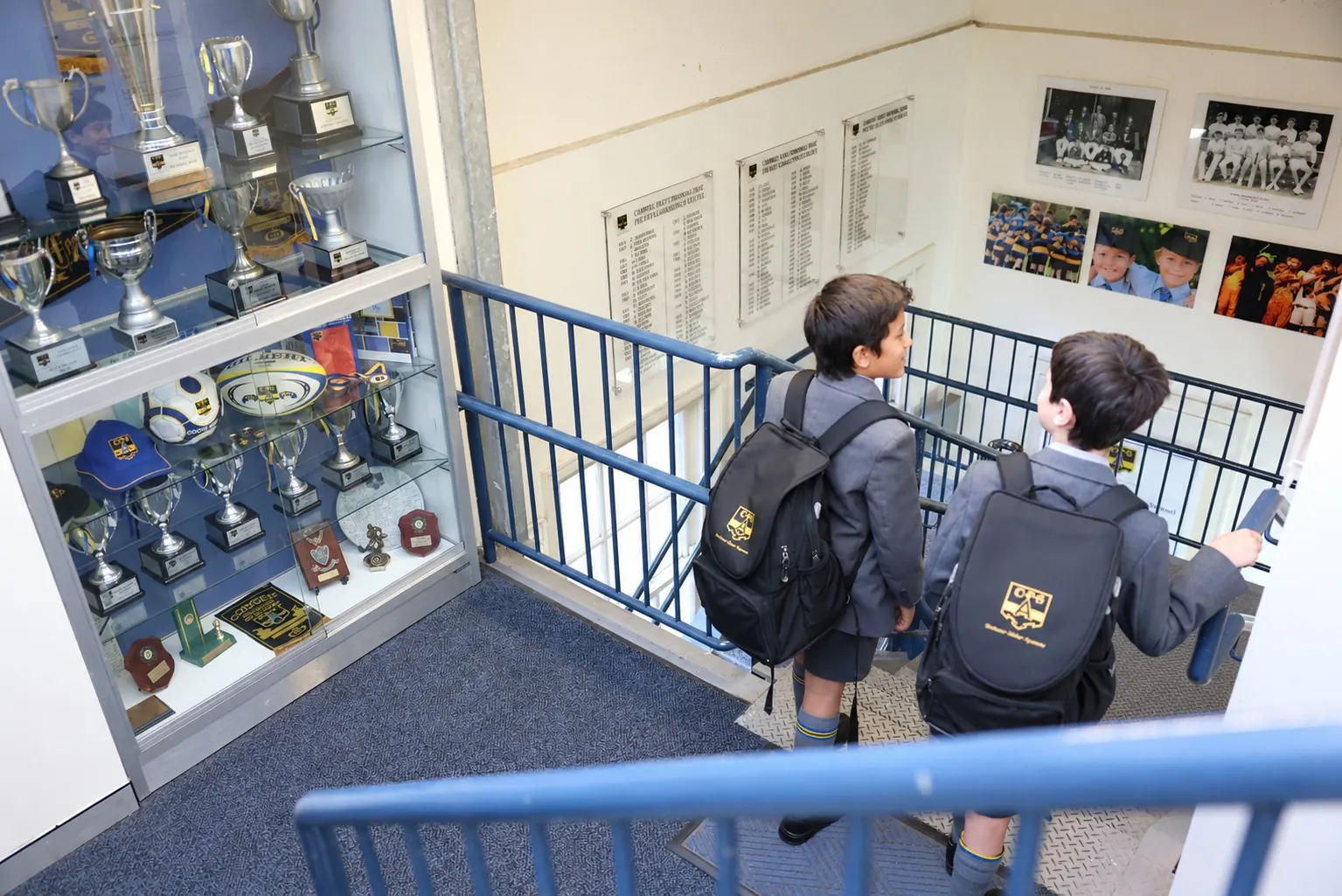 Two Coogee Prep boys with their school bags on the stairs beside the trophy cabinet