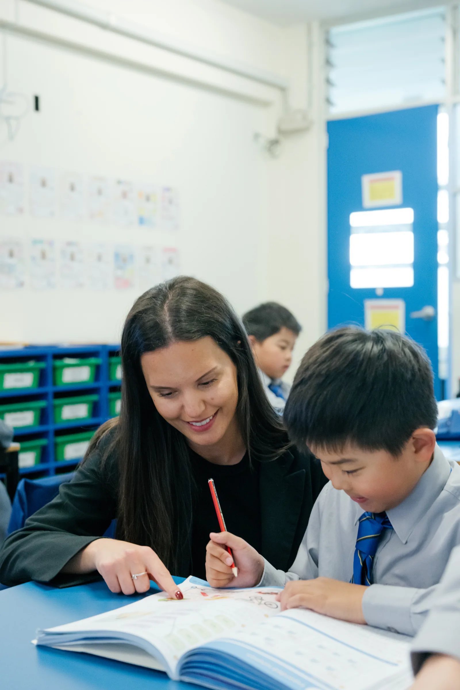 A Coogee Prep teacher helping a boy with his reading at his desk