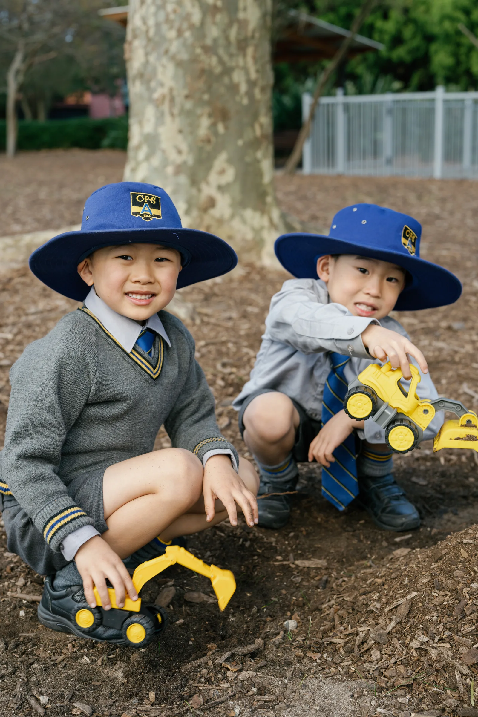 Two Coogee Prep boys in school hats playing with toy diggers outdoors