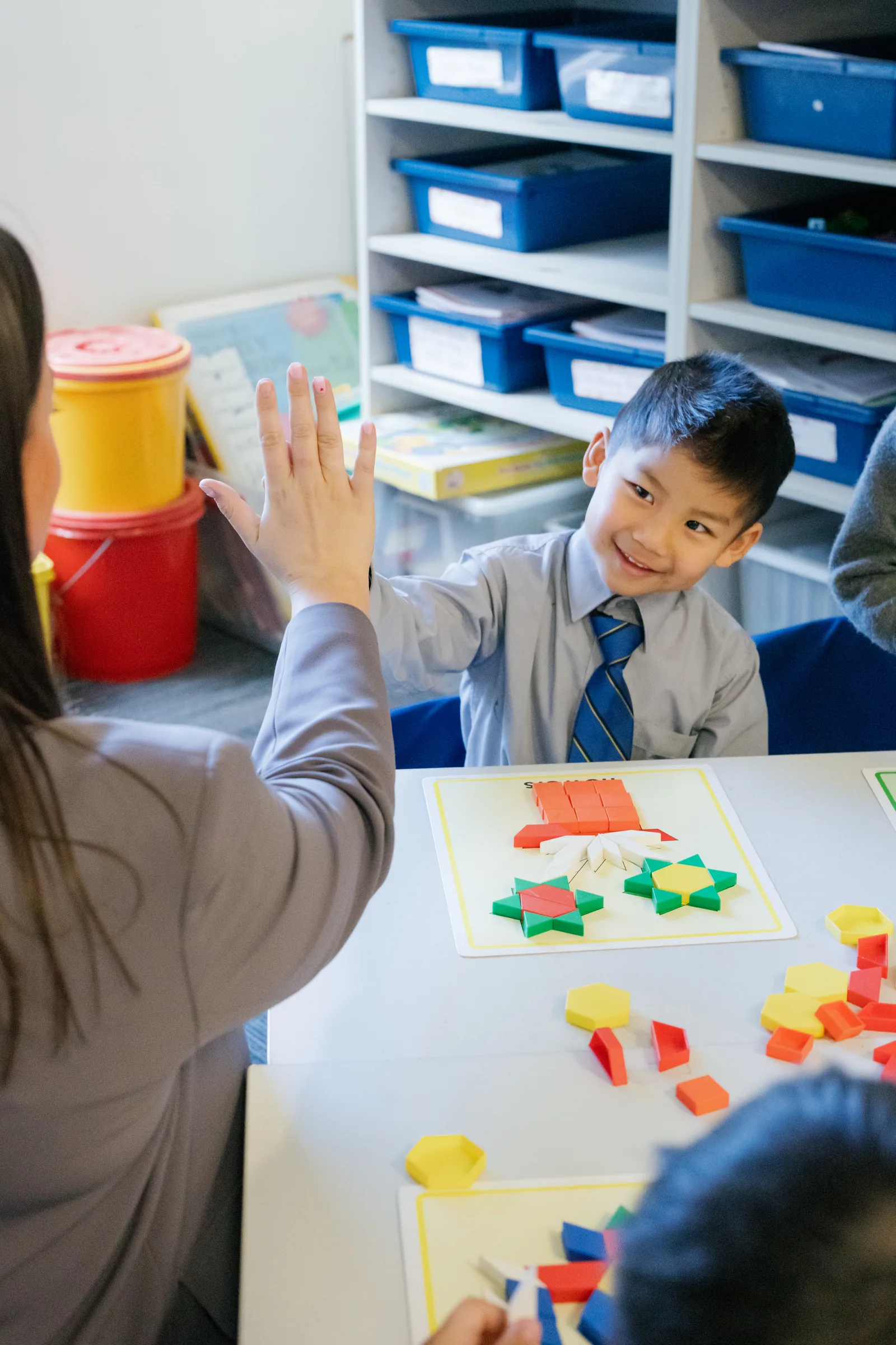A Coogee Prep boy high-fiving his teacher over a pattern-block maths activity