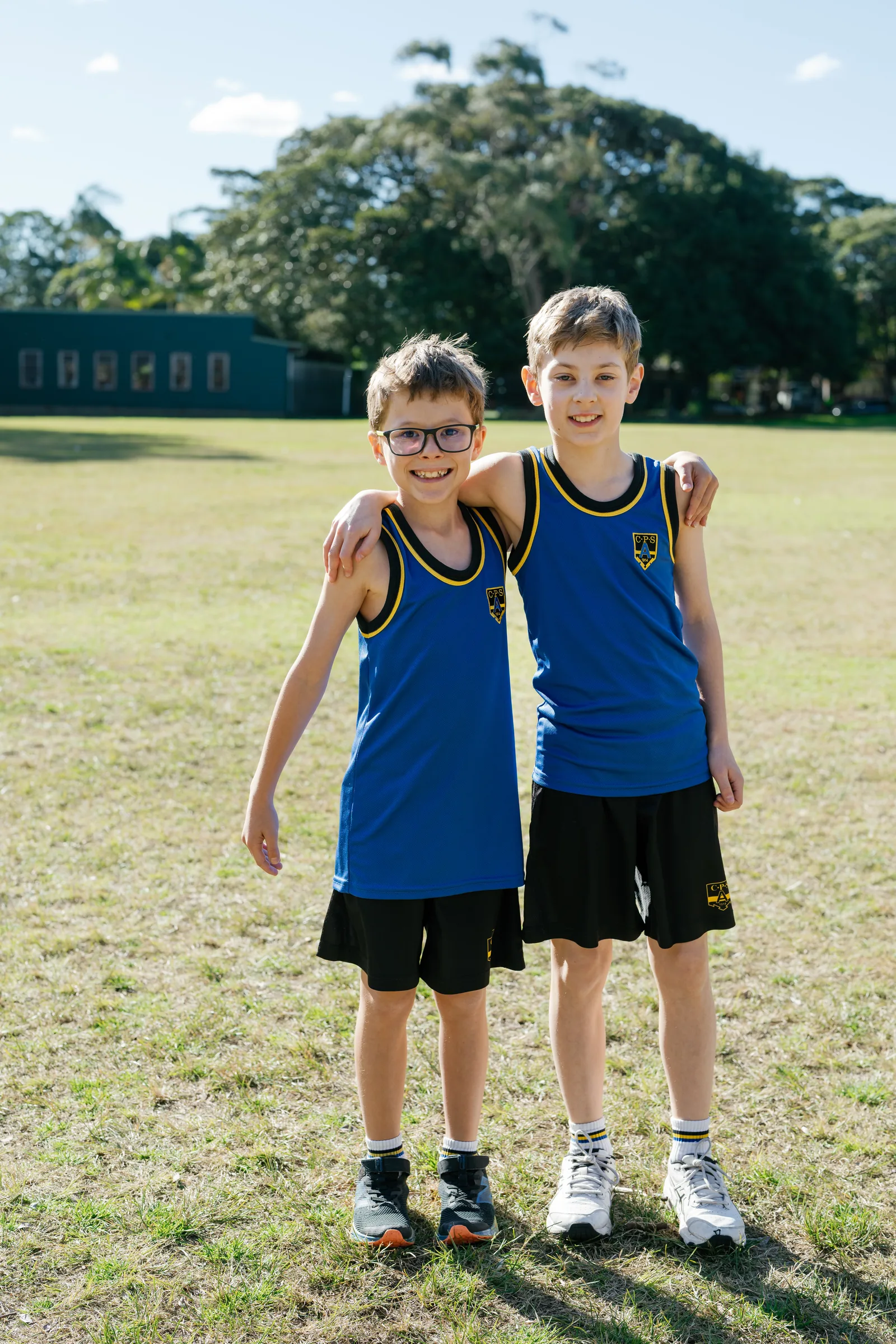 Two Coogee Prep boys in sports uniform with their arms around each other on the oval